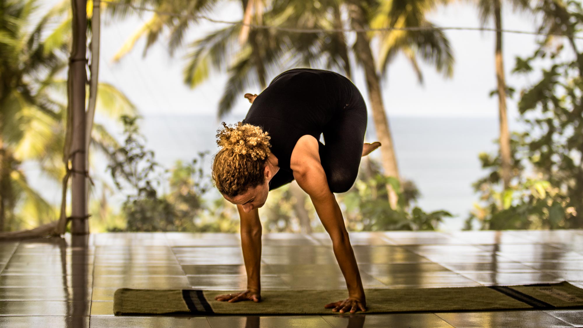 Joanna the co-founder of Alpha Yoga School in arm balance near the beach in India