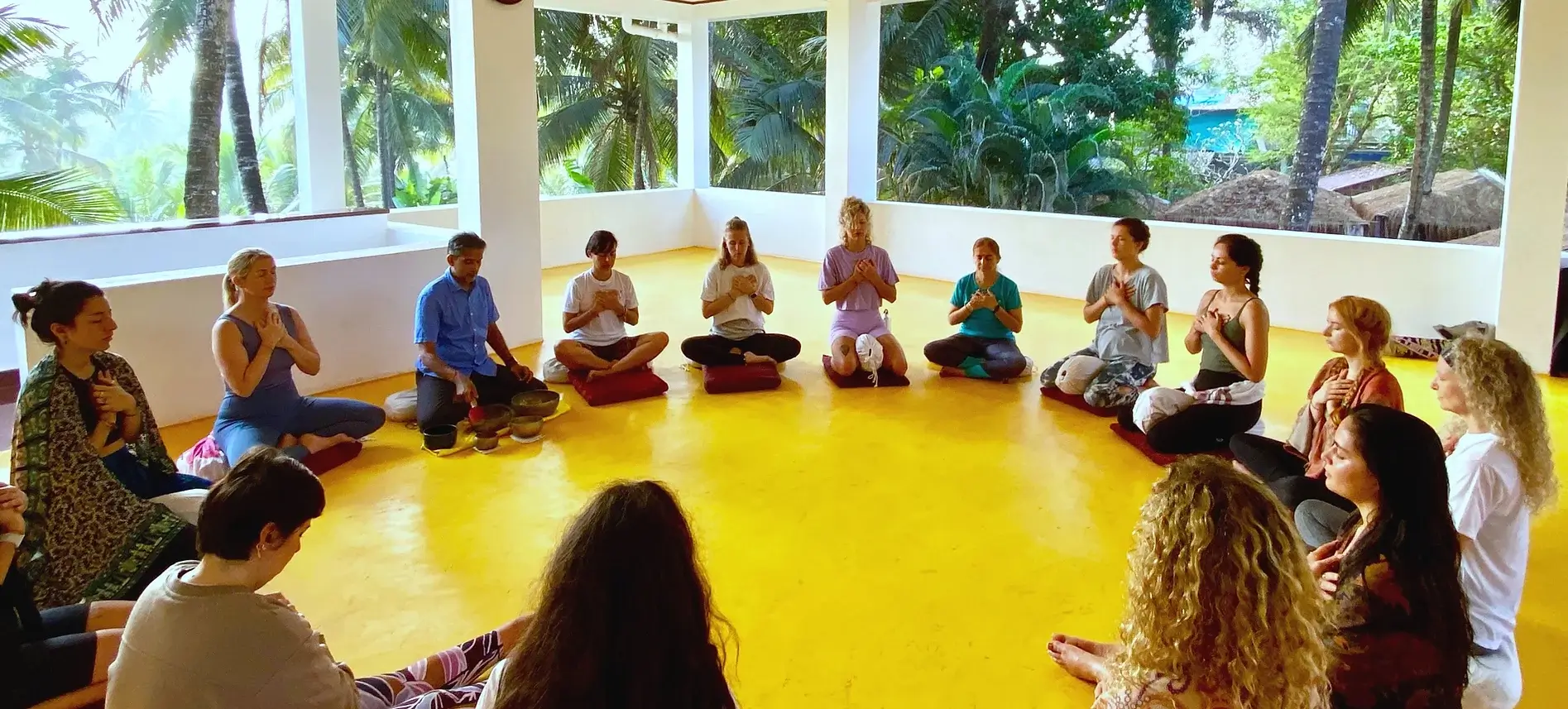 Yoga students sit in a circle with hands on their heart