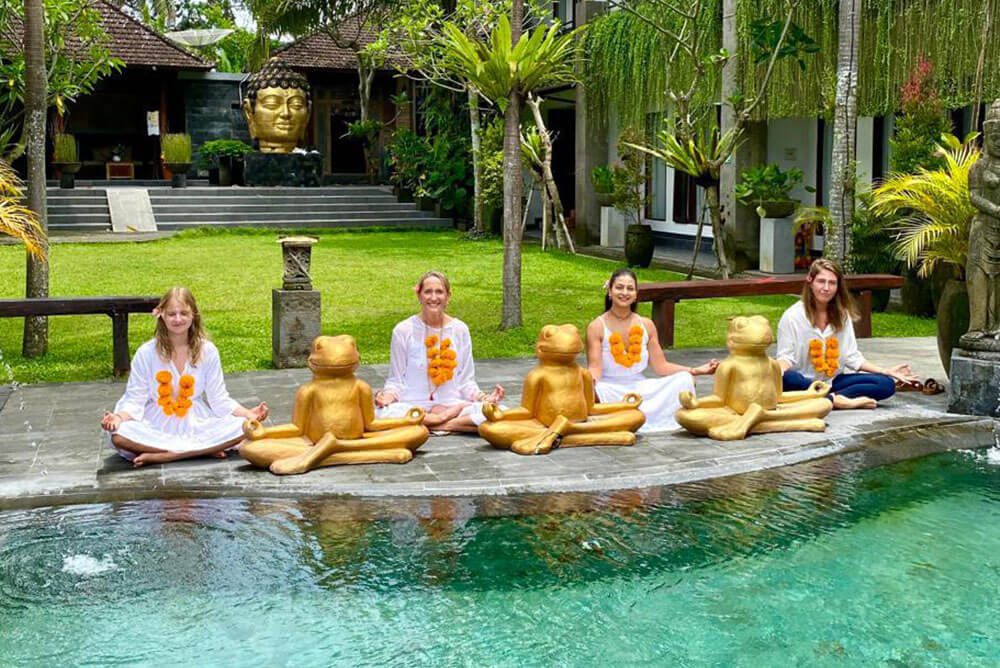Yoga students of Maa Shakti in Bali sitting with white clothes and flower malas in a cross legged posture by the pool during their yoga teacher training.