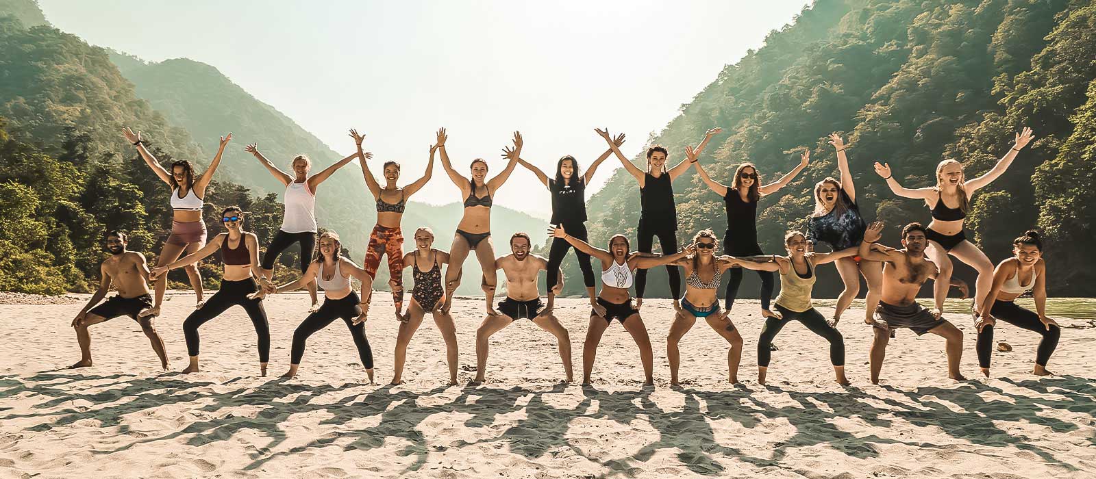 Yoga students lined up on the beach posing for a picture with their fellow students during a yoga teacher training in Rishikesh, India.