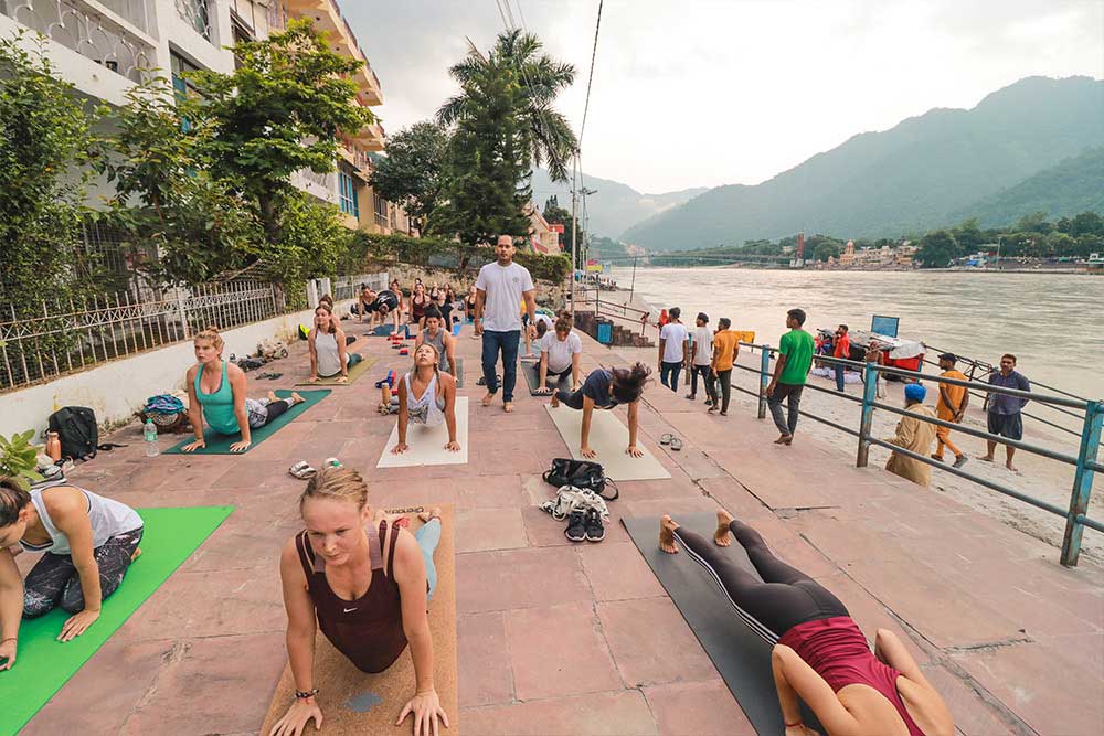Yoga students practicing outside by the river in Rishikesh, India during their yoga teacher training with Rishikesh Vinyasa Yoga School.