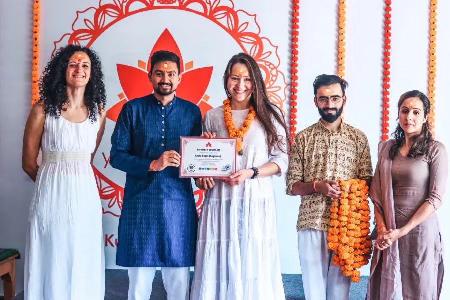 A yoga student taking a picture with her teachers and certification after graduating from her 200H yoga teacher training in Rishikesh, India.