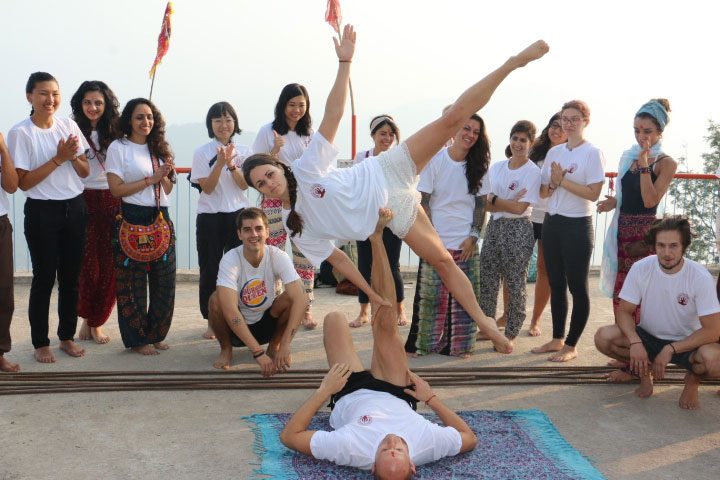 yoga students posing and smiling in white t-shirts after graduating from their yoga teacher training in Rishikesh, India.